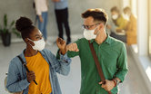 College students with masks elbow bump in hallway